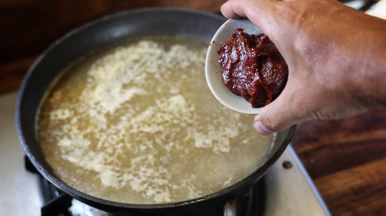 adding gochujang to skillet of broth