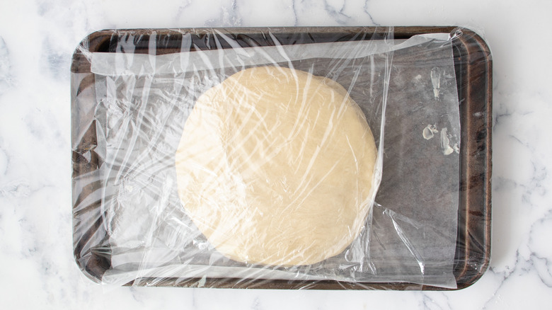 Flat dough disks stacked on baking sheet covered with plastic wrap