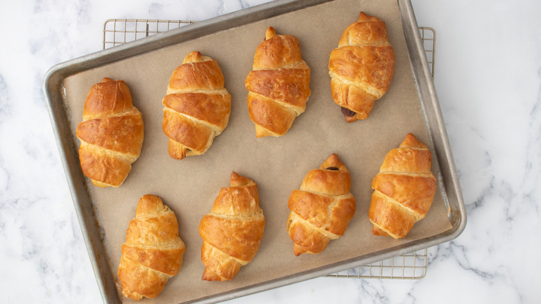 Baked croissants cooling on baking sheet and rack