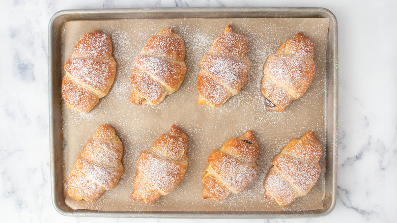 Powdered sugar dusted croissants on baking sheet