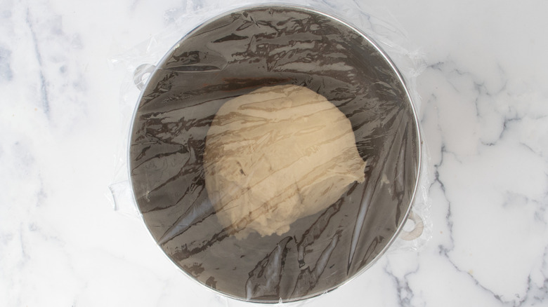 Dough in plastic wrap covered bowl