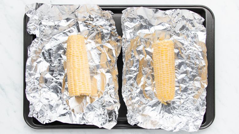 Buttered ears of corn in foil on baking sheet