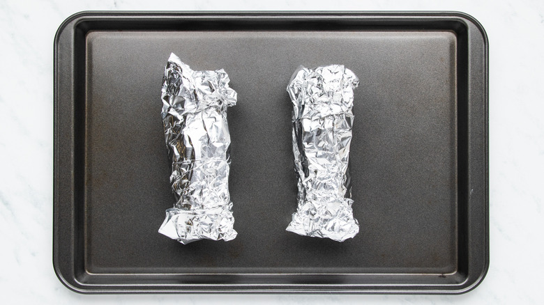 Corn wrapped in foil on baking sheet