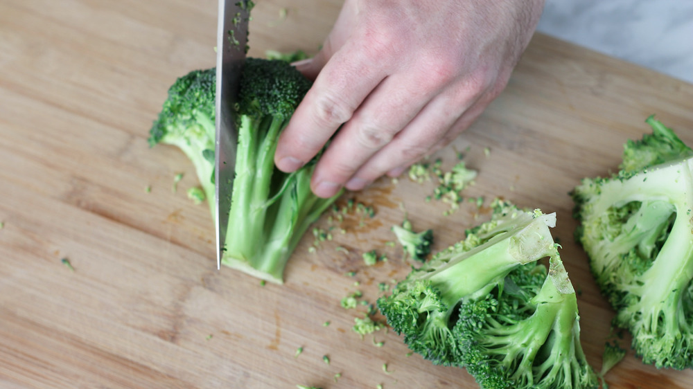 chopping broccoli on cutting board to make roasted vegetables