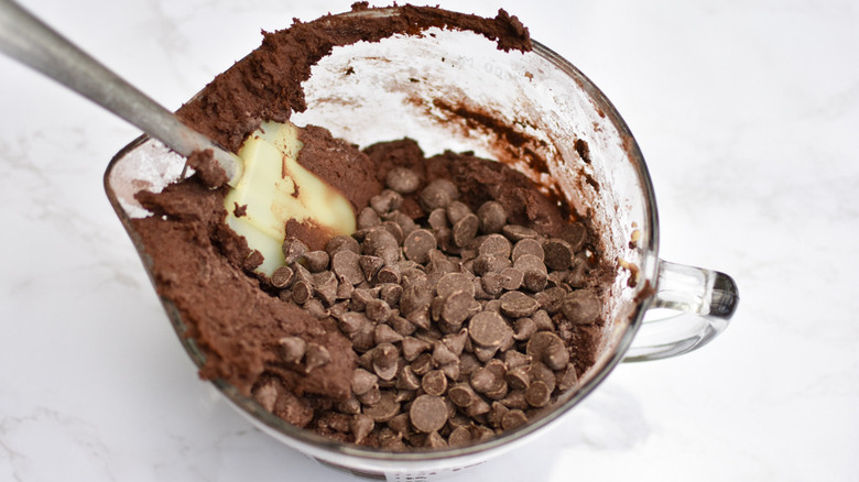 A spatula sitting in a clear container filled with chocolate cookie dough and chocolate chips