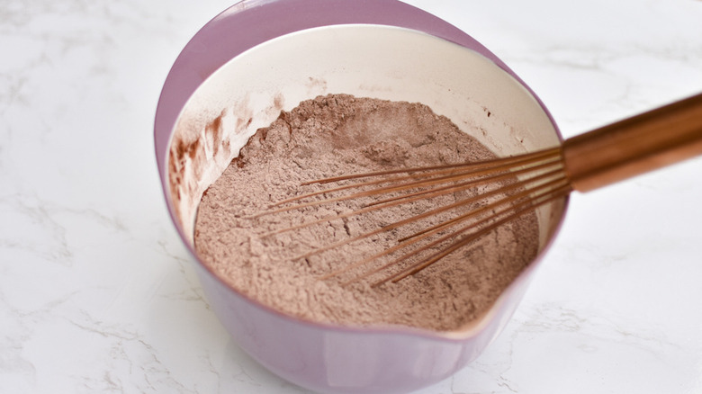 A whisk sitting in a bowl half full of flour, cocoa, salt, and baking soda