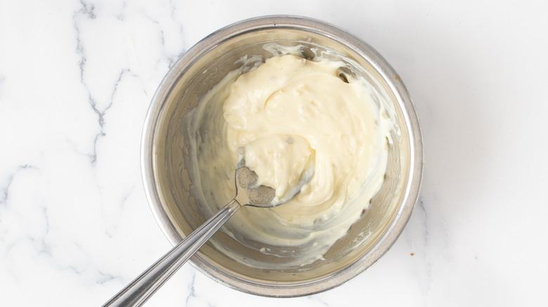 stirring sauteed garlic with mayo in bowl