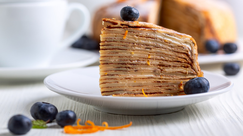 a slice of crepes suzette cake on a plate with fresh blueberries