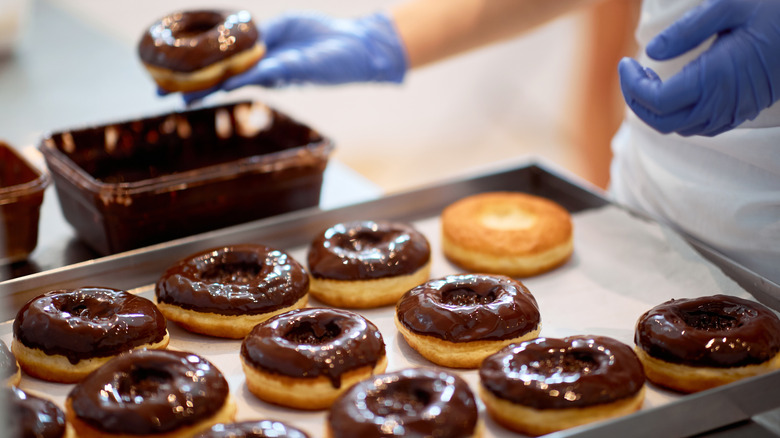 person dipping freshly made donuts in chocolate glaze in a professional kitchen