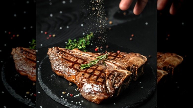 person seasoning steak with pepper