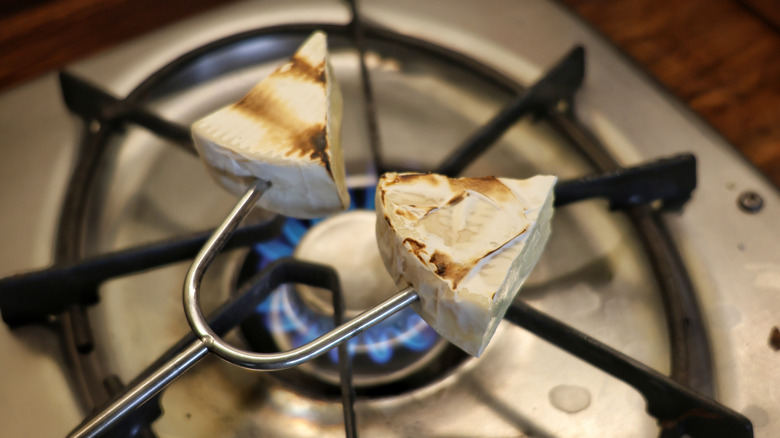 two pieces of brie on skewer roasting over gas stove flame