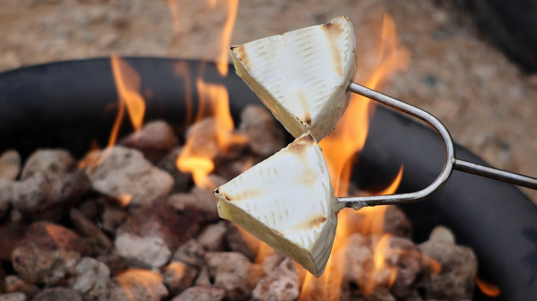 two pieces of brie on skewer roasting over open fire