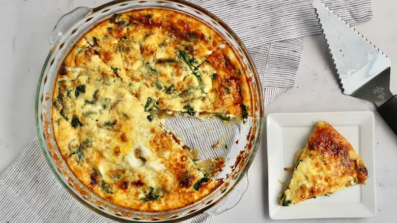 Round pie dish with spinach quiche with slice out. 