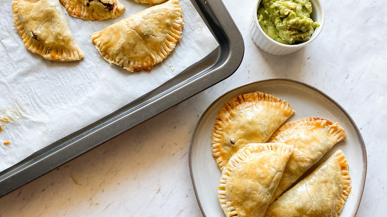 Baked empanadas on plate with bowl of guacamole.