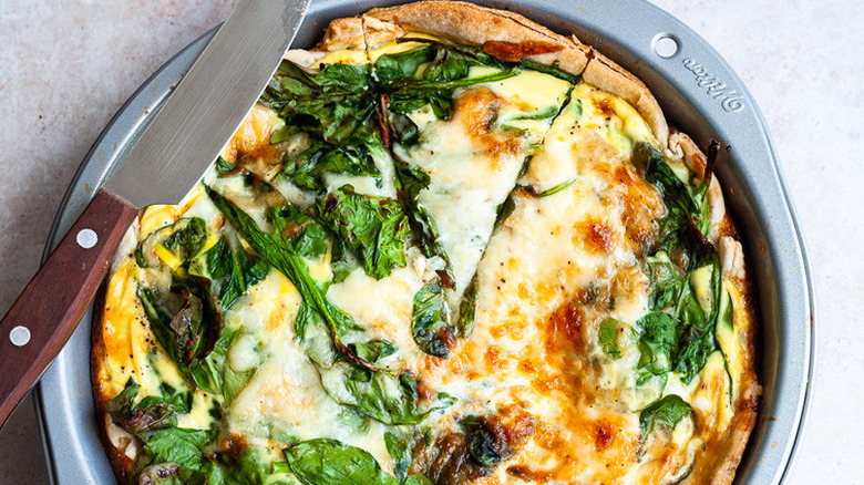 Baking pan with spinach quiche, with slice cut. 