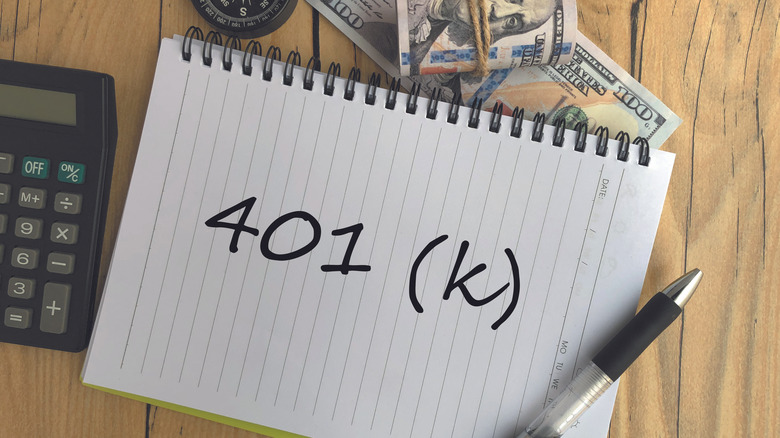 401(k) written on notebook with pen, money, and calculator nearby