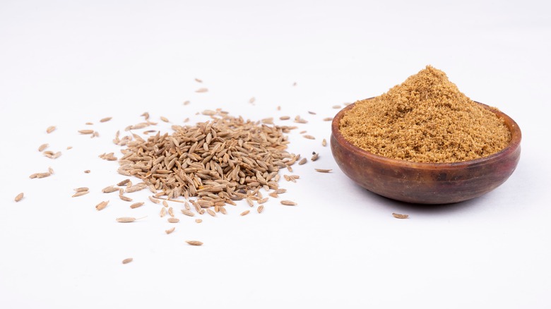 Cumin seeds next to bowl of ground cumin