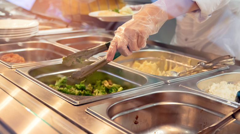 school cafeteria worker grabbing food with tongs