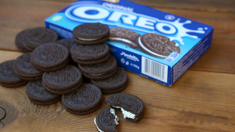 Box of Oreos on wooden background with Oreos piled alongside