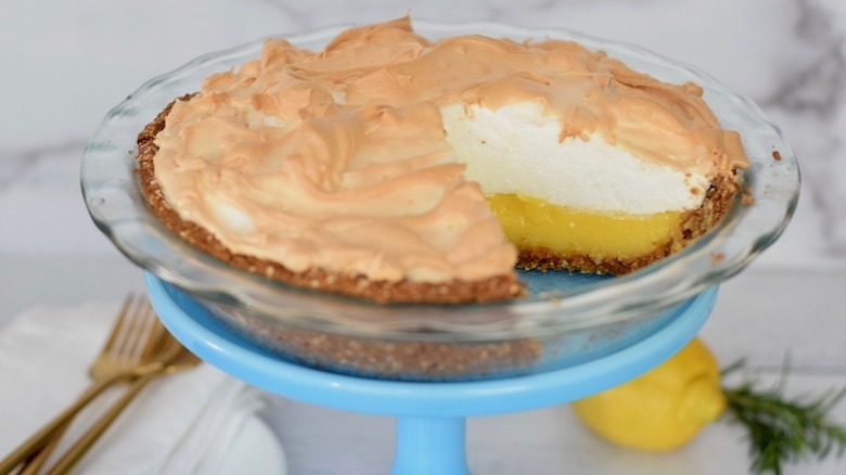 bright yellow lemon meringue pie in a glass pie plate on a blue cake stand