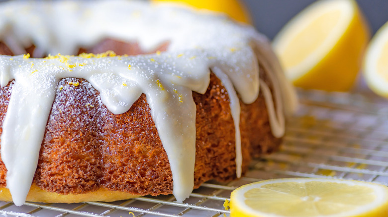 lemon bundt cake covered with a lemony glaze on a cooling rack with lemon slices nearby