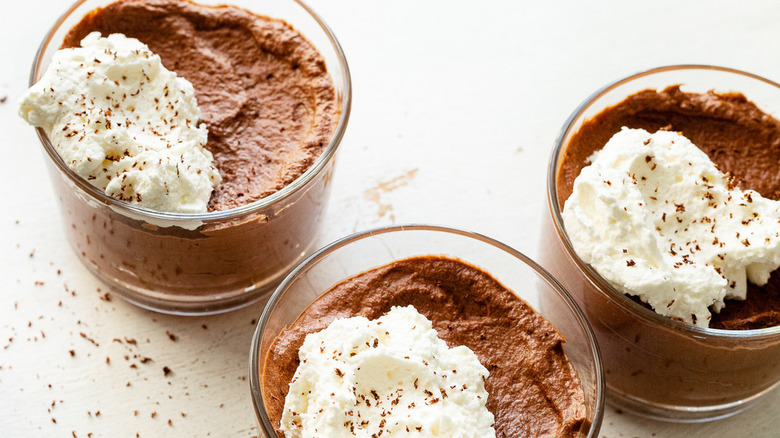 three glass cups of chocolate mousse topped with a dollop of whipped cream and chocolate shavings