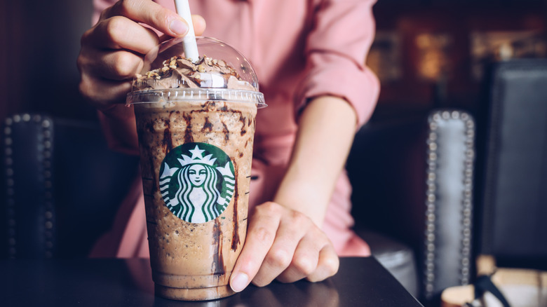 blended chocolate drink with whipped cream, someone stirring it in the background