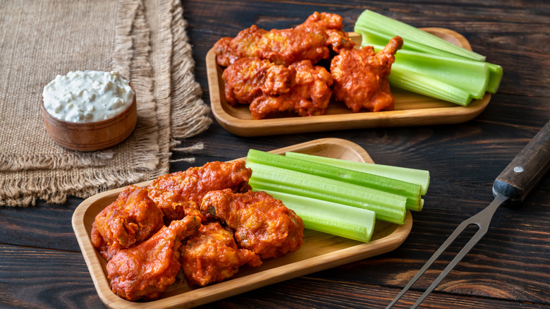 two trays of buffalo wings with celery and a side of blue cheese