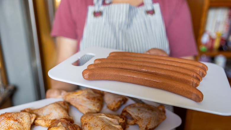 Woman holding raw hot dogs and chicken 