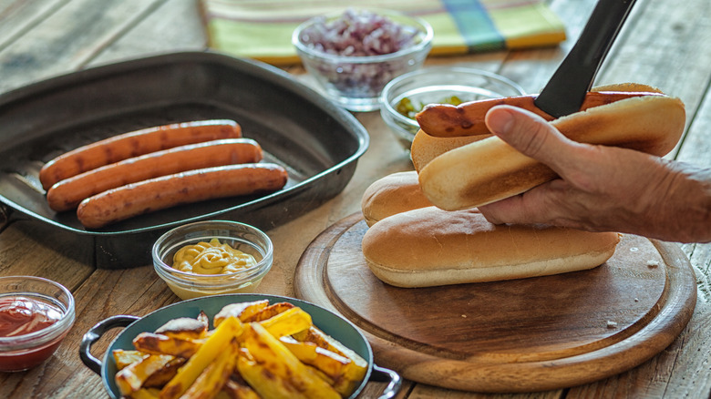 Taking hot dog from grill pan and putting it in bun