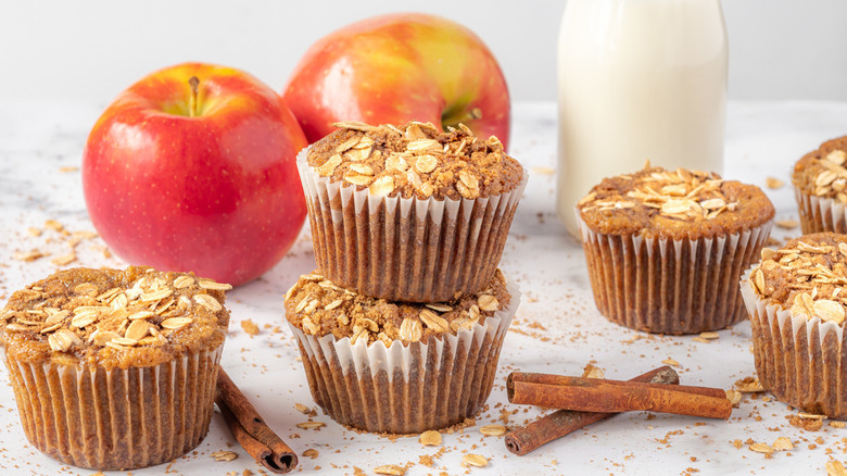 apple cinnamon muffins topped with oatmeal and milk and apples in the background