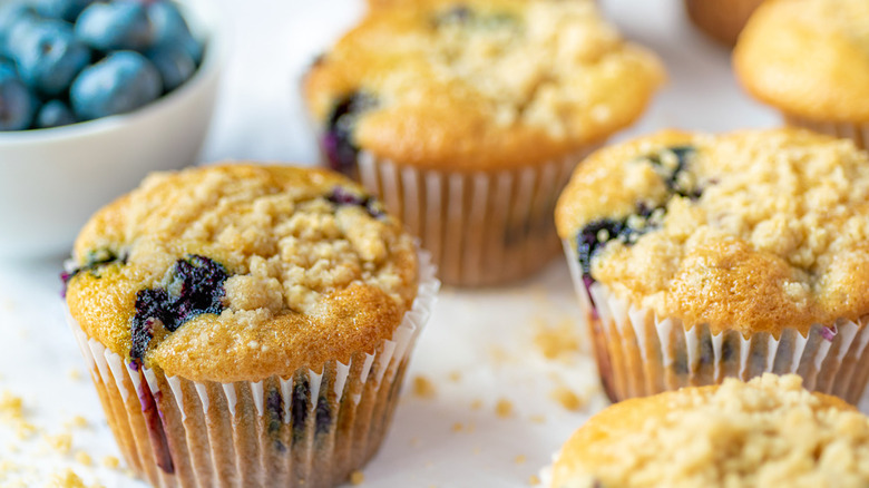 blueberry muffins in wrappers with a bowl of blueberries