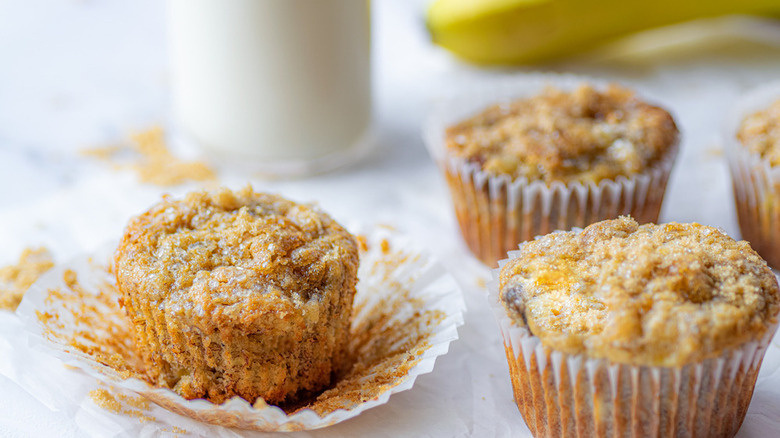 banana muffins in wrappers with a glass of milk and a banana