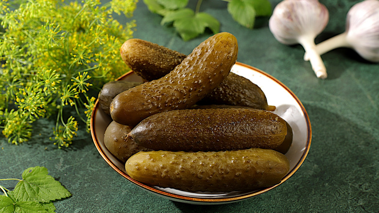 bowl of dill pickles with garlic and fresh dill in the background