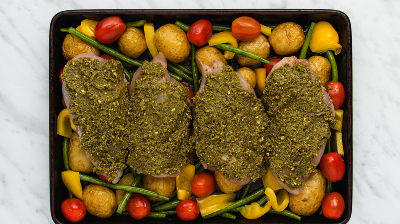 Chicken breasts covered with pesto in prepared pan with vegetables