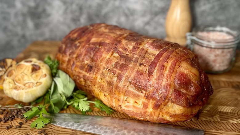 Bacon-wrapped turducken with roastedgarlic on a cutting board with knife