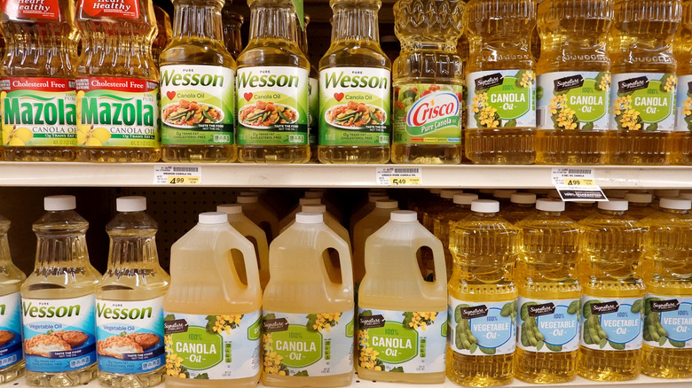 Store shelf lined with bottles of canola oil and vegetable oil.