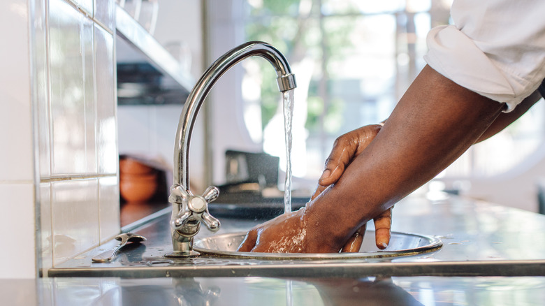 Hands washing up at sink in bright kitchen.