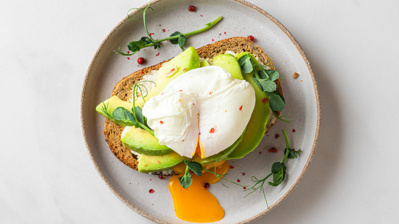 avocado toast topped with runny egg and watercress