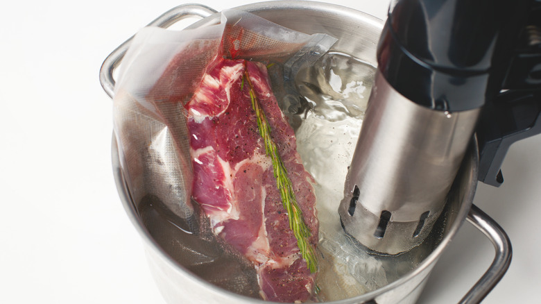 Raw steak and rosemary in a plastic bag cooking in a pot of water sous vide. 