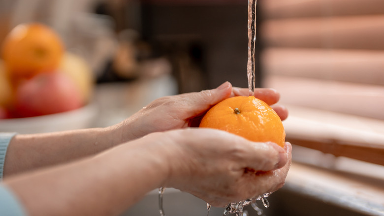 hands washing orange in sink