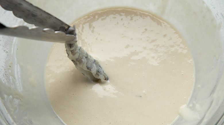 tongs dipping shrimp in batter