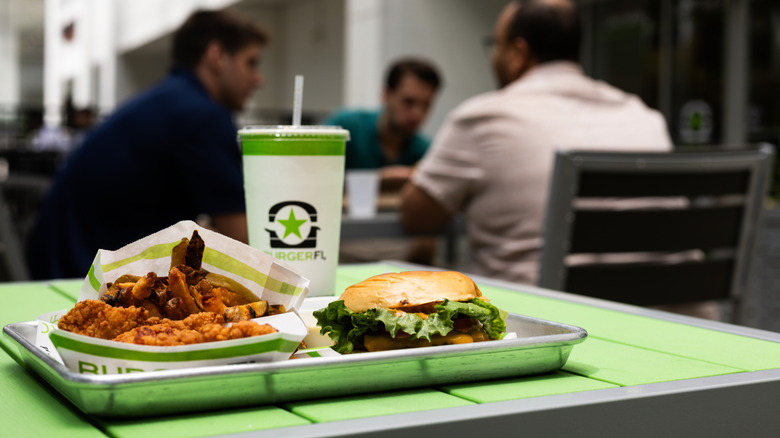 Burger, fries, chicken, drink on green table