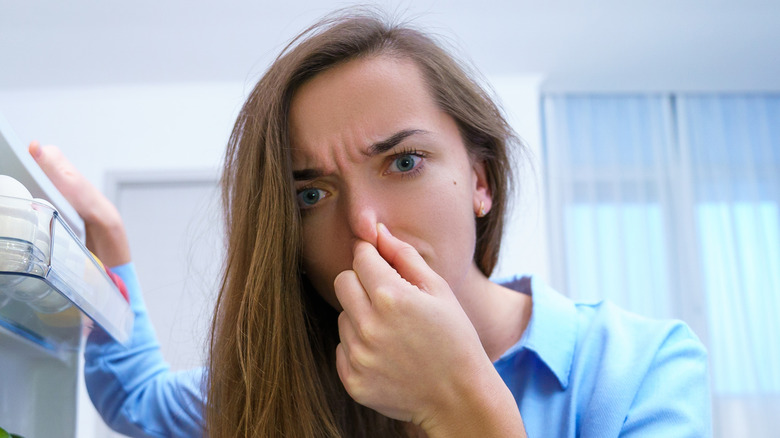 woman holding nose while opening fridge door