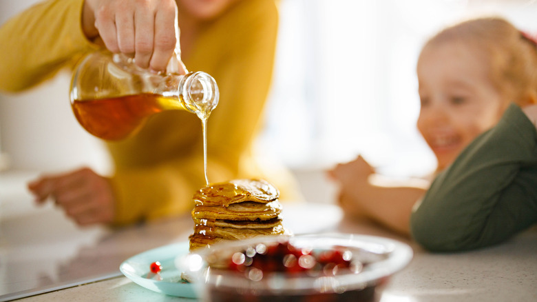 person pouring syrup over pancakes