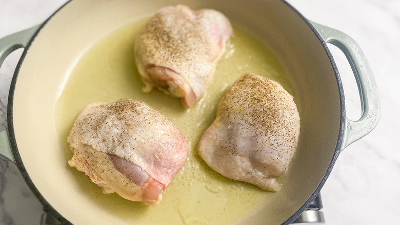 raw chicken thighs in a pan with oil sprinkled with pepper