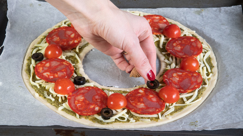 hand placing olive on pizza