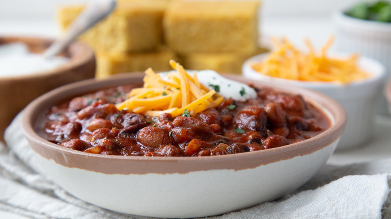 bean chili in a bowl topped with shredded cheese and sour cream and served with cornbread