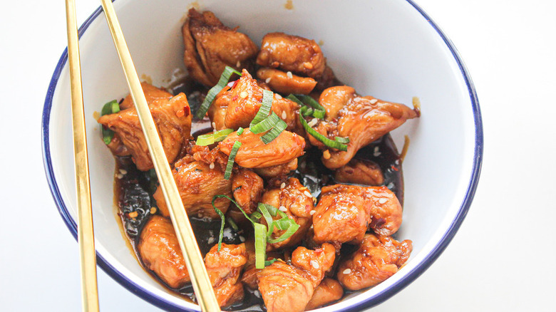 teriyaki chicken in a bowl with garnish and chopsticks