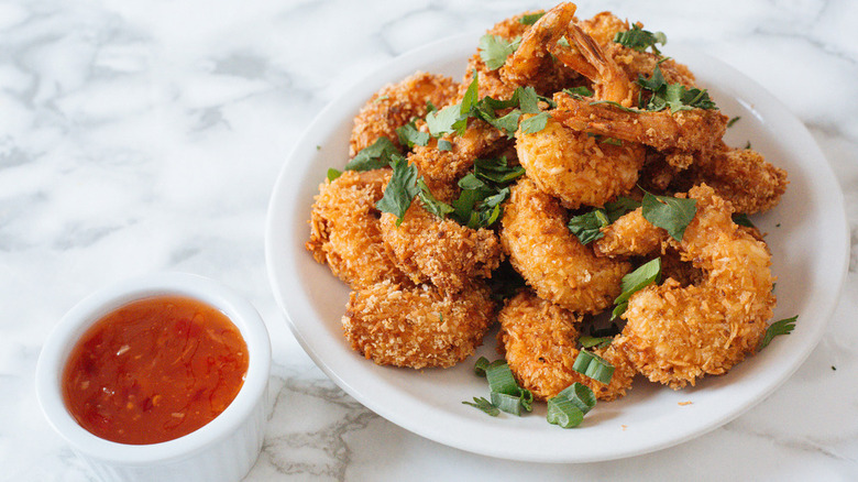 several coconut shrimp on a plate with green onions and a side of dipping sauce